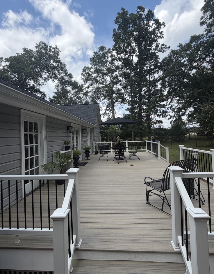 Newly built light-tan composite deck with white railing and black balusters attached to the back of a one-story house, with a dining set and patio umbrella